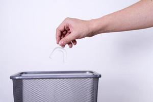 una mano arroja protectores bucales dentales a un bote de basura contra un fondo gris. foto