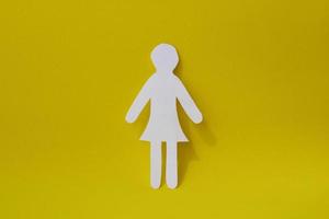 Silhouette of a woman in dress of white paper, cut by hand. In the center of the photo on yellow background