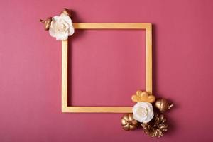 Square golden frame blank with flowers and golden hearts on red background. Flat lay, top view, copy space photo