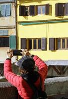 Florence, Italy, 2019 - Chinese tourists line up to take a photo of the famous Ponte Vecchio with their smartphones.