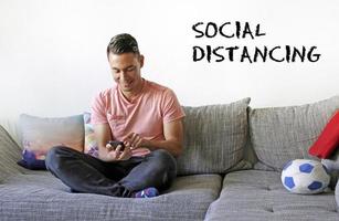 hombre sonriente escribiendo en un smartphone con las palabras distanciamiento social a su lado foto