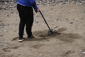 hombre con detector de metales buscando tesoros en la playa foto