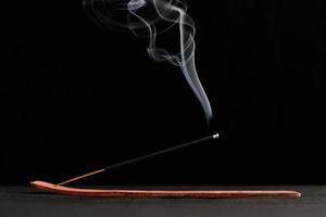 Smoke curls of burning incense stick in wooden holder for relaxation and meditation black background photo