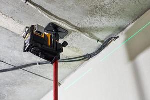 Laser level measuring tool with visible green laser beam on wall for installing stretch ceiling photo