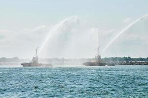 Tug boats spraying jets of water, demonstrating firefighting water cannons, fire boats spraying foam photo