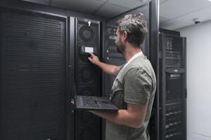 Data Center Engineer Using Laptop Computer Server Room Specialist Facility with Male System Administrator Working with Data Protection Network for Cyber Security or Cryptocurrency Mining Farm. photo
