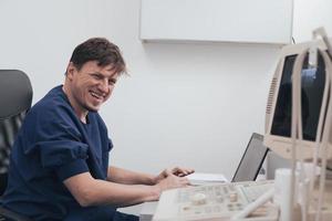 Orthopedist doctor examining X-ray picture at desk in clinic on laptop computer photo