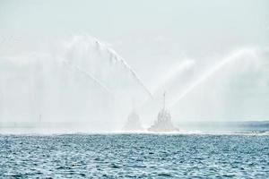 Tug boats spraying jets of water, demonstrating firefighting water cannons, fire boats spraying foam photo