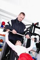 .man assisting woman weitght lifting at a gym photo