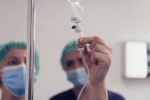 General practitioner holding intravenous drip infusion. Doctor handling IV fluid drip with copy space on white background. Nurse performing Intravenous therapy. photo