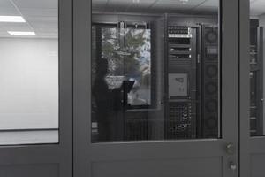 Software Engineer Working on a Laptop Computer in a Modern Server room. Monitoring Room Big Data Scientist in reflection of the entrance door. photo