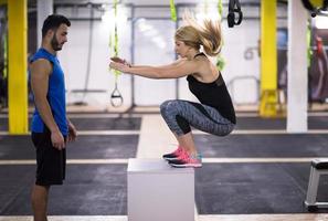 woman working out with personal trainer jumping on fit box photo