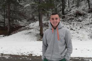 A portrait of a young man in a snowy forest dressed in casual clothes. Selective focus photo