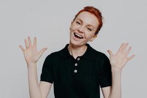 Young excited red haired woman raising palms and exclaiming loudly, isolated over grey background photo