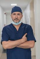 Portrait Of Mature Male Doctor In Busy Modern Hospital Corridor. photo