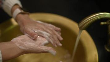 mulher lava as mãos na pia dourada e torneira