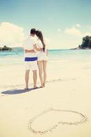 romantic  couple in love  have fun on the beach with heart drawing on sand photo