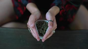Woman hold small ceramic container of loose leaf green tea during tea ceremony video