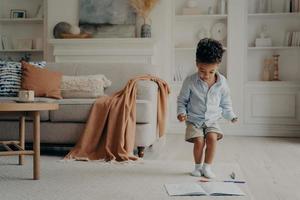 Happy mixed race little boy enjoying playing alone at home, having fun in living room photo