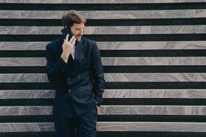 Businessman in elegant black clothes phones to partner focused down keeps smartphone photo