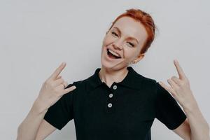 Cheerful carefree ginger female in casual clothes showing heavy metal rock sign photo