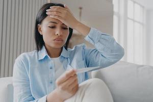 mujer malsana sufre de gripe gripal o coronavirus con termómetro, midiendo la temperatura foto