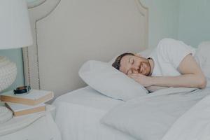 Young relaxed bearded man lying in bed with closed eyes photo