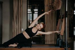 bella mujer haciendo ejercicio y estirándose en cadillac reformer foto