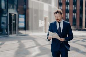 Successful businessman in formal wear reads newspaper while walking