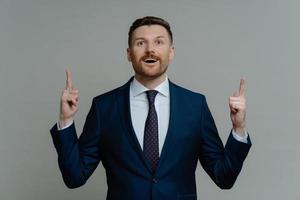 Shocked businessman in suit pointing up with fingers and looking with amazed face expression photo