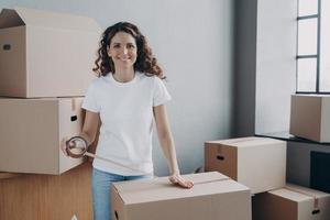 European lady is wrapping cardboard boxes with packing tape. Moving service worker. photo