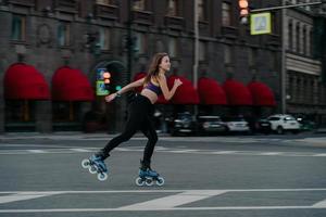 Extreme sport recreation and fitness activity concept. Active woman rides on rollers in urban environment strengthens leg muscles demonstrates high level of stability balances on small wheels photo