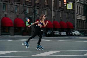 concepto de actividad física y recreación deportiva extrema. mujer activa monta sobre rodillos en el entorno urbano fortalece los músculos de las piernas demuestra un alto nivel de equilibrio de estabilidad en ruedas pequeñas foto