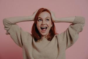 Surprised shocked european female holding head in hands and looking upside with excited expression photo