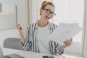 Successful female manager plans budget checks finances makes fist pump holds paper documents photo