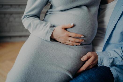 Cropped shot of unrecognizable parents await for baby. Pregnant woman with big belly poses on husbands hands feels child movement in abdomen. Parenthood concept photo