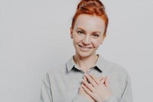 Headshot of young grateful ginger holding hands on chest, feeling love and appreciation photo