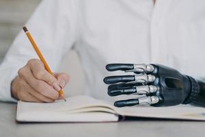 Cyber arm and healthy limb on the notebook. Woman with bionic prosthesis is studying remotely. photo