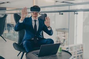 Businessman in formal suit and in VR headset glasses pointing with open palms up in air photo