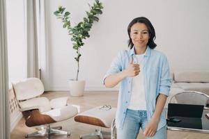 Female employee recommends work in her company, shows thumb up approval hand gesture at office photo