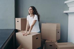 Hopeful woman is packing cardboard box. Happy hispanic girl purchasing real estate and moving. photo