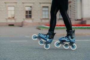 mujer irreconocible en patines azules se mueve en la carretera pasa tiempo libre intenta activamente nuevos ejercicios tiene poses de entrenamiento al aire libre cerca de un edificio antiguo. patinar como hobby. Estilo de vida activo foto