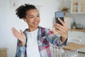 Young mixed race girl blogger holds smartphone use video call, greeting followers in social network photo