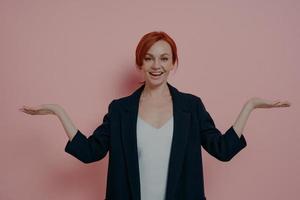 Cheerful positive young ginger woman comparing two options, standing isolated on pink background photo