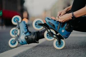 Horizontal shot of faceless woman puts on rollerskates rides on road poses against urban background involdved in active sport. People hobby recreation extreme sport active lifestyle concept. photo