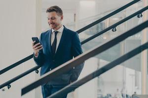 Businessman in formal suit using smartphone while standing on staircase photo