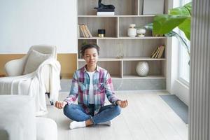 la adolescente afro está practicando yoga en casa y ejerciendo la posición de loto. el alivio del estrés.