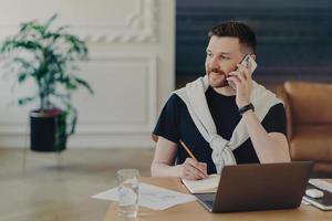 Pleasant freelancer talking on mobile phone while working from home photo