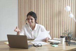 Happy italian female tutor in headset conducts webinar online on laptop in modern home office photo