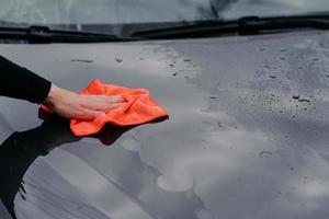 Cleaning car using microfiber cloth. Man washes black auto hood. Polishing vehicle. Car detailing, maintenance photo